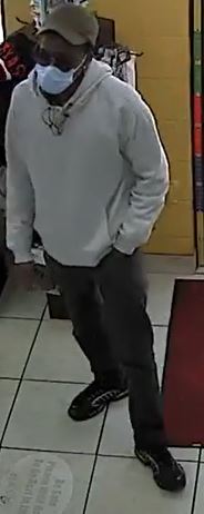 Image of second suspect at location dressed in a light gray hoodie, tan baseball hat, dark pants with silver and black shoes. 